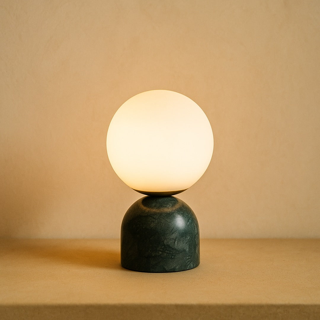 Pearl opal glass globe lamp on a green marble base against warm cream plaster