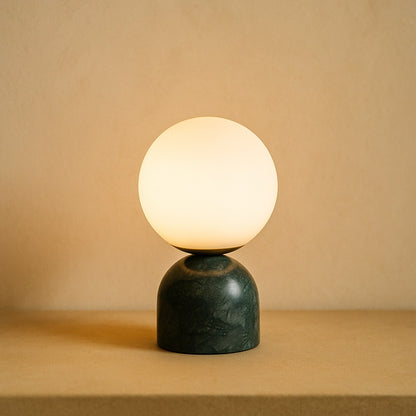 Pearl opal glass globe lamp on a green marble base against warm cream plaster