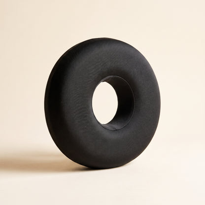Ring™ Ear Relief Pillow — charcoal donut pillow with centre ear hole on warm cream background
