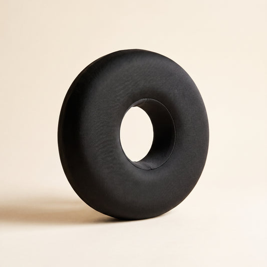 Ring™ Ear Relief Pillow — charcoal donut pillow with centre ear hole on warm cream background