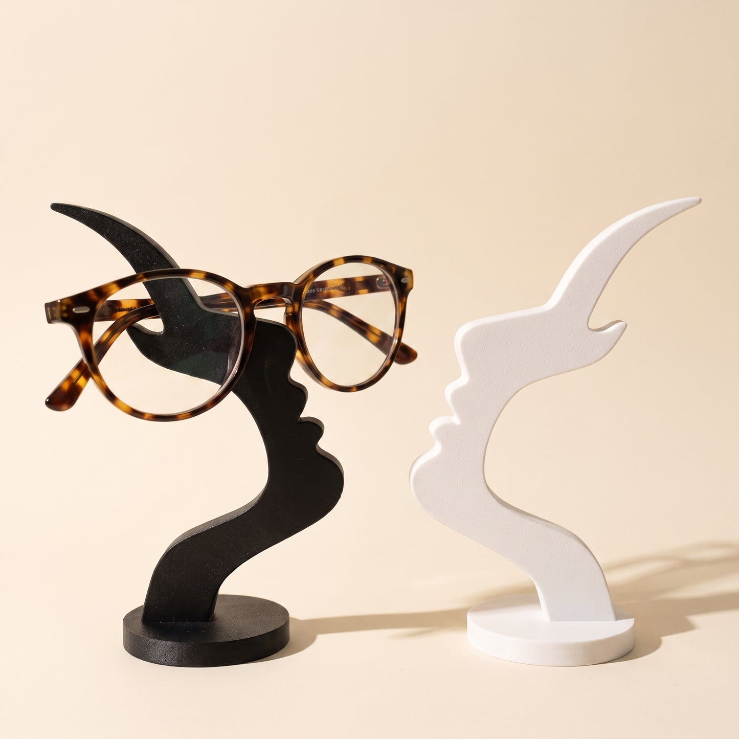 Visage™ Glasses Stand — black and white face-profile stands on warm cream background