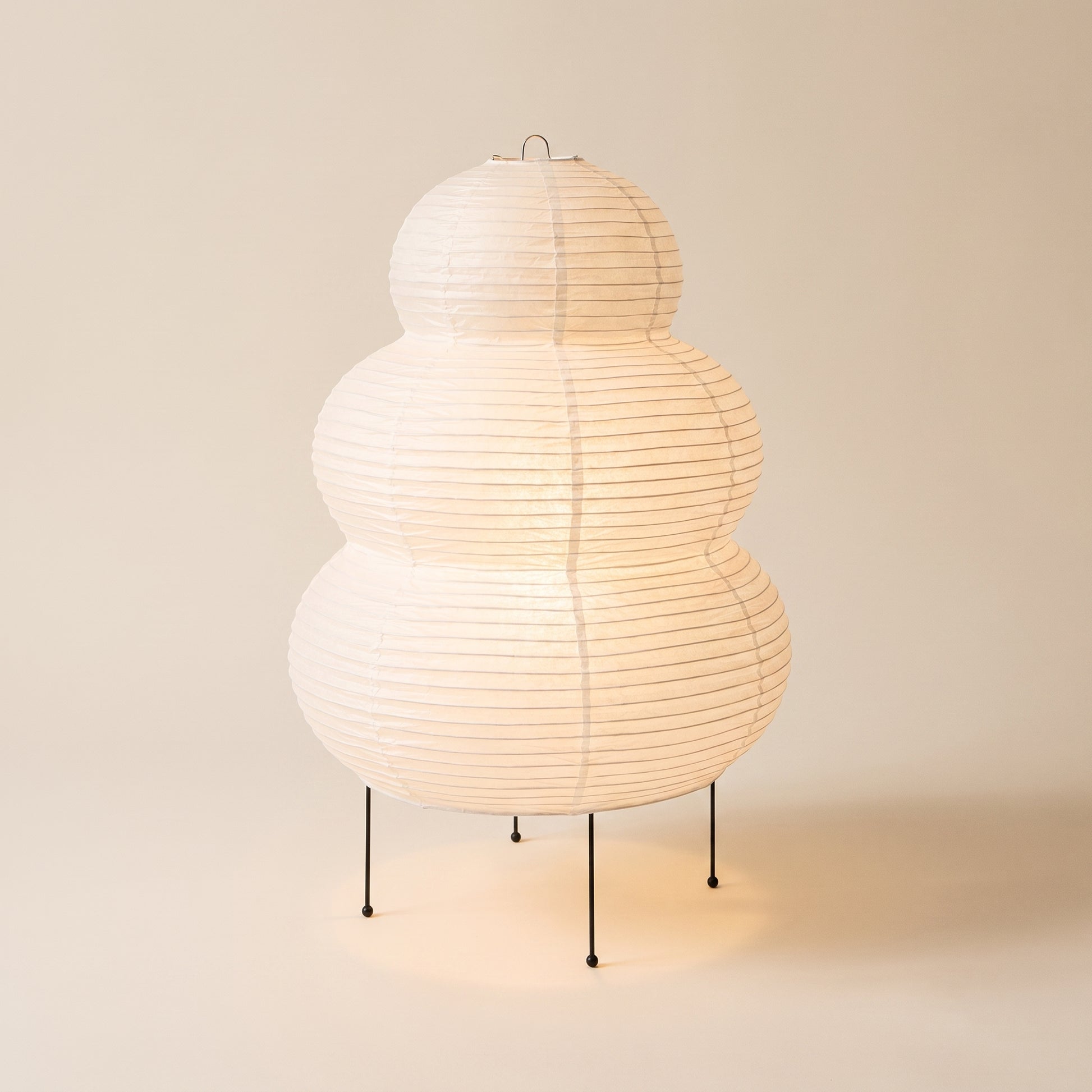 Cocoon™ Paper Table Lamp — triple-tier rice-paper lamp glowing on warm cream background
