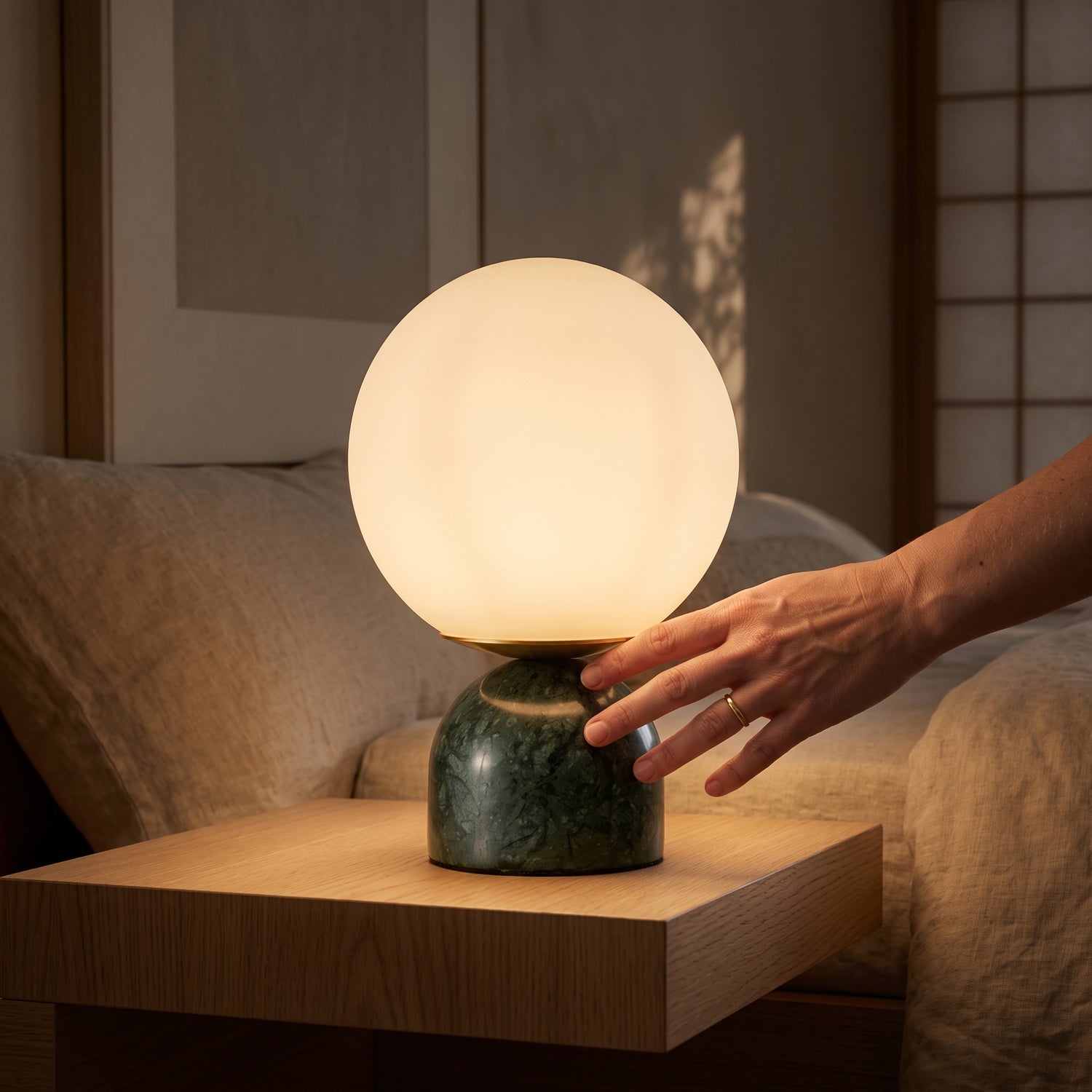 A hand reaching to switch on the Cobble™ Marble Lamp beside a bed at night