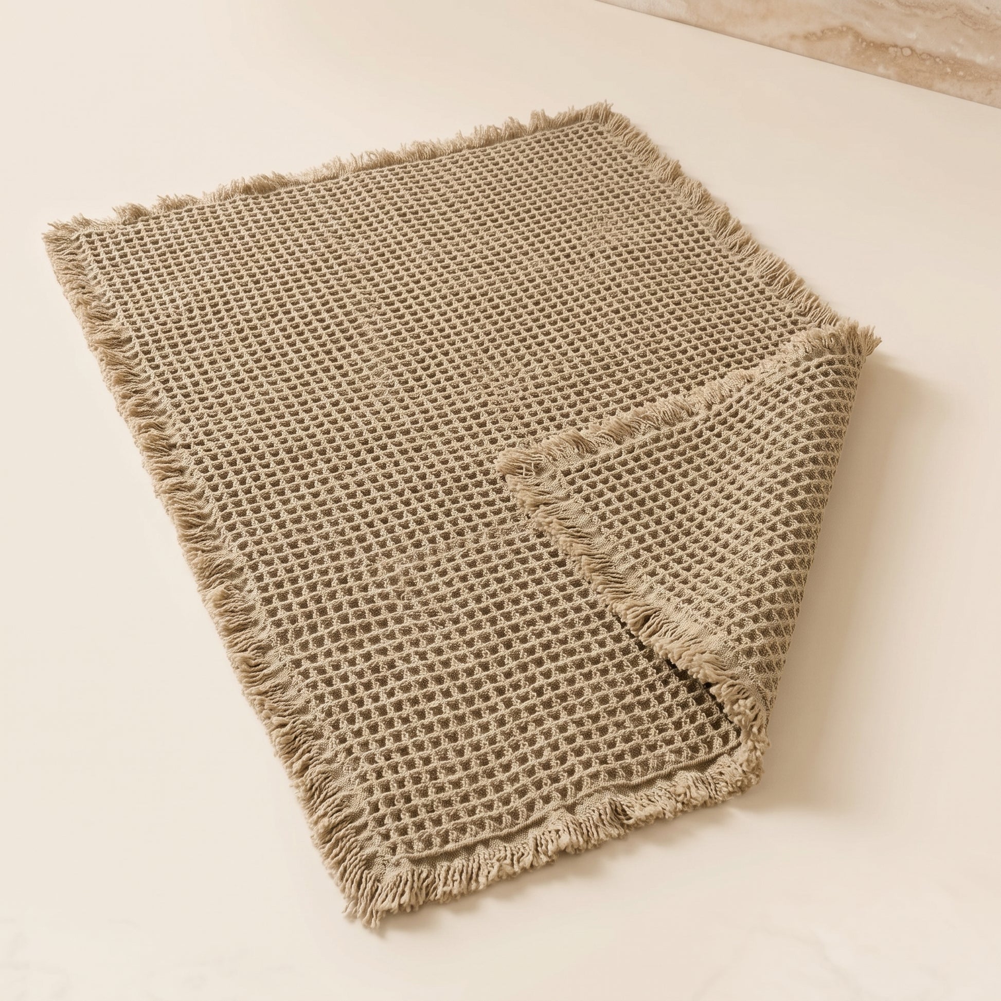 Waffle™ Bath Mat — greige waffle-weave mat with fringed ends on warm cream background