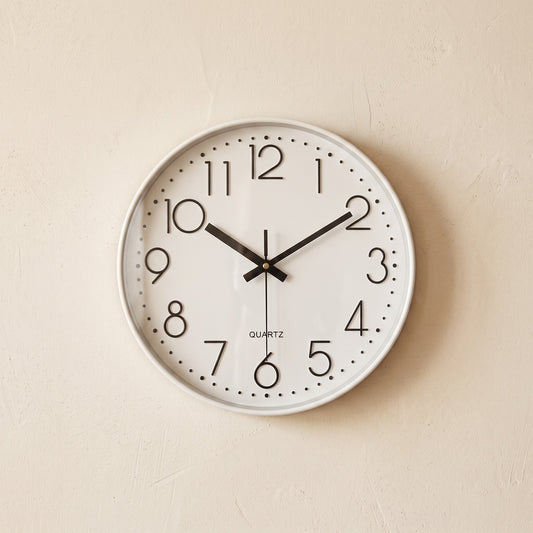 Hush Clock in All White hanging on a warm cream plaster wall
