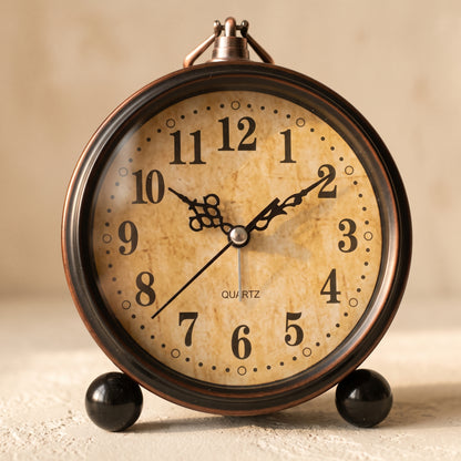 Patina aged-bronze bedside alarm clock on a warm cream plaster surface