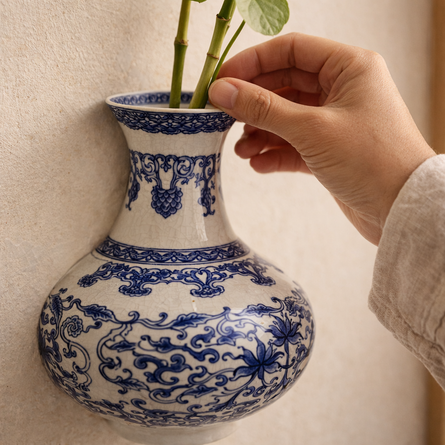 A hand lowering lucky bamboo stems into the flared mouth of the Indigo™ wall vase