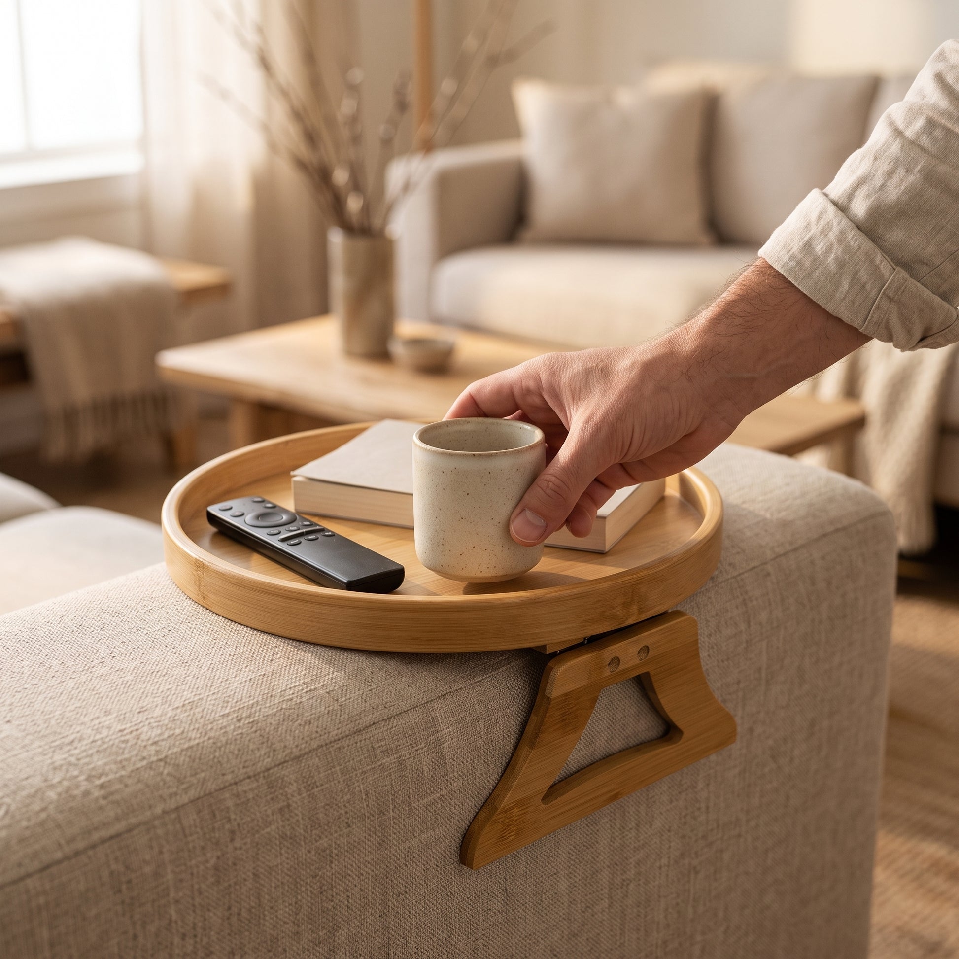 A hand setting a mug down onto the Saddle™ tray on a sofa arm