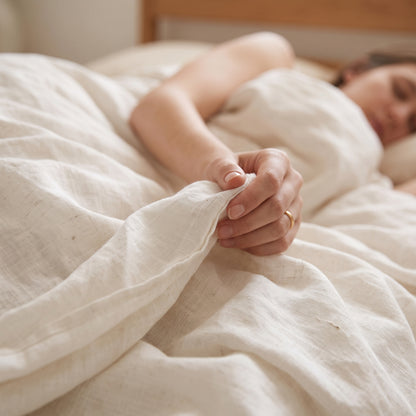 Woman drawing the white linen flat sheet up over her shoulder in bed