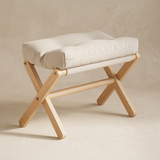 Threshold folding stool in chalk, pale wood X-frame with a tufted cushion, on warm cream plaster
