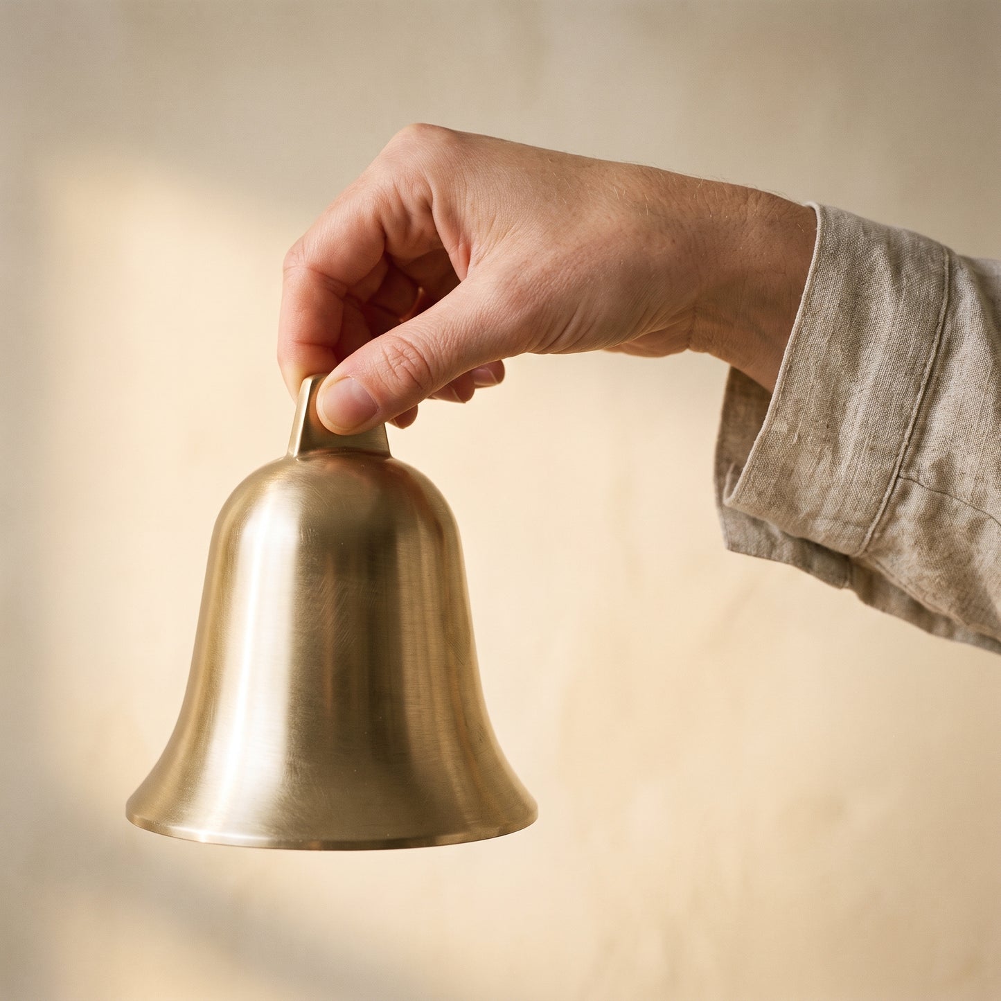 A hand lifting the Vesper brass bell by its pierced crown tab
